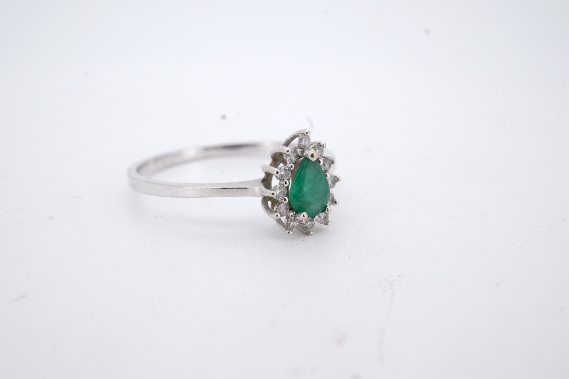 A modern white metal(stamped 14k), emerald and diamond set pear shaped cluster ring, size R, gross weight 1.3 grams.